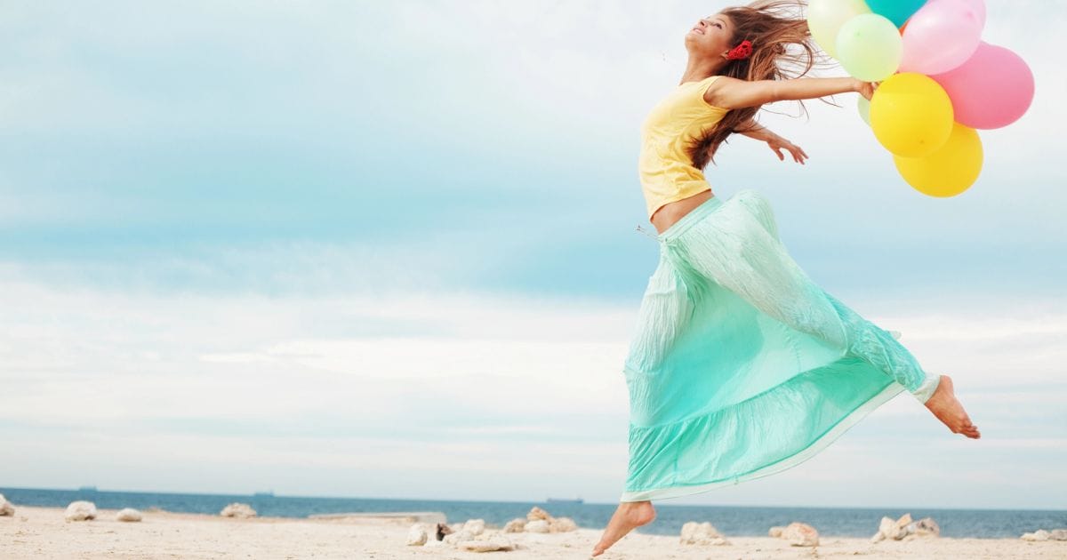 donna che salta leggera in spiaggia con dei palloncini in mano