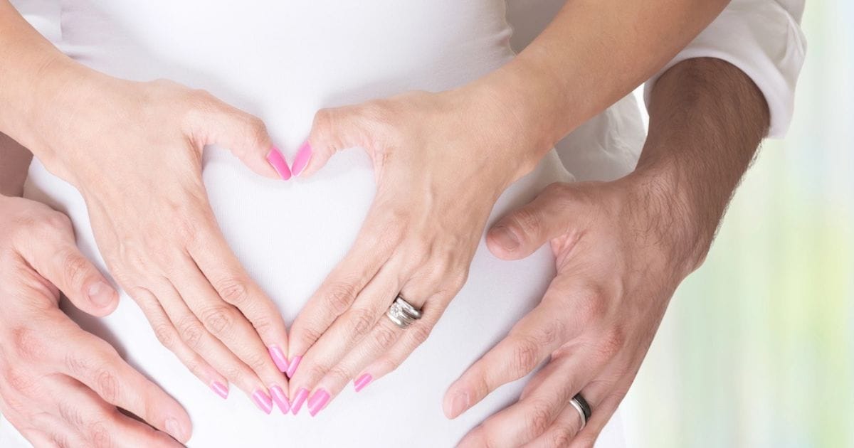 uomo e donna con le mani a forma di cuore sulla pancia